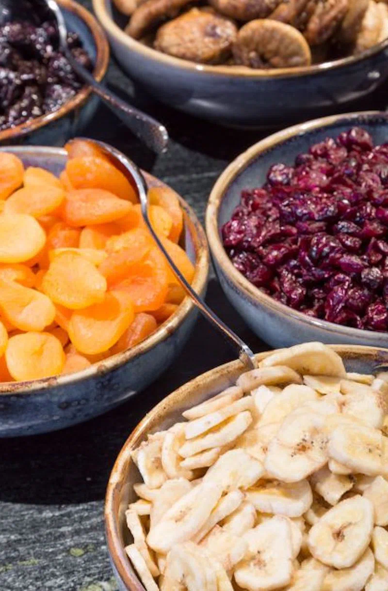 Verschiedene Trockenfrüchte wie Aprikosen, Bananen und Cranberries in Schalen.